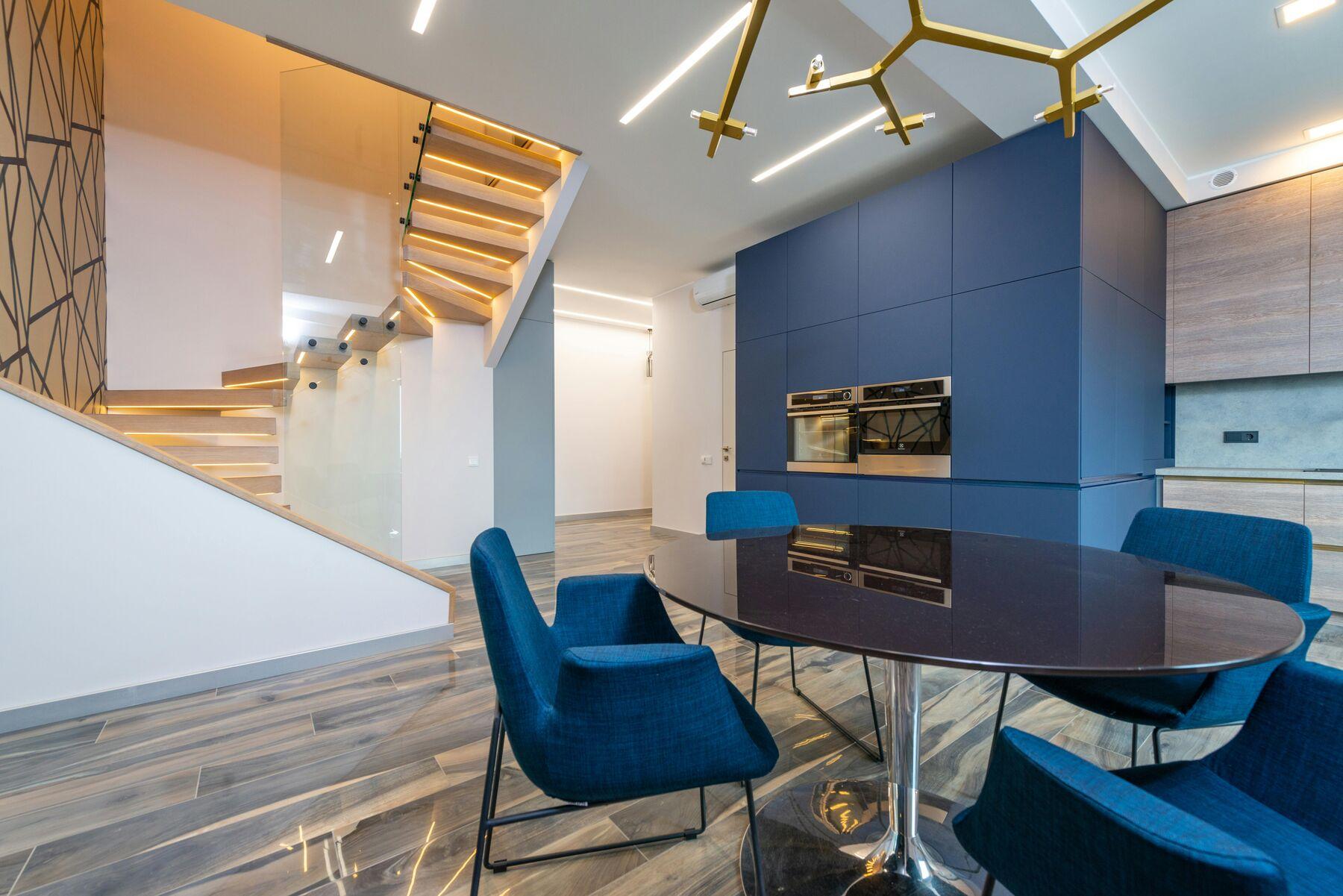 Modern dining space with a gold branch chandelier and LED-lit staircase