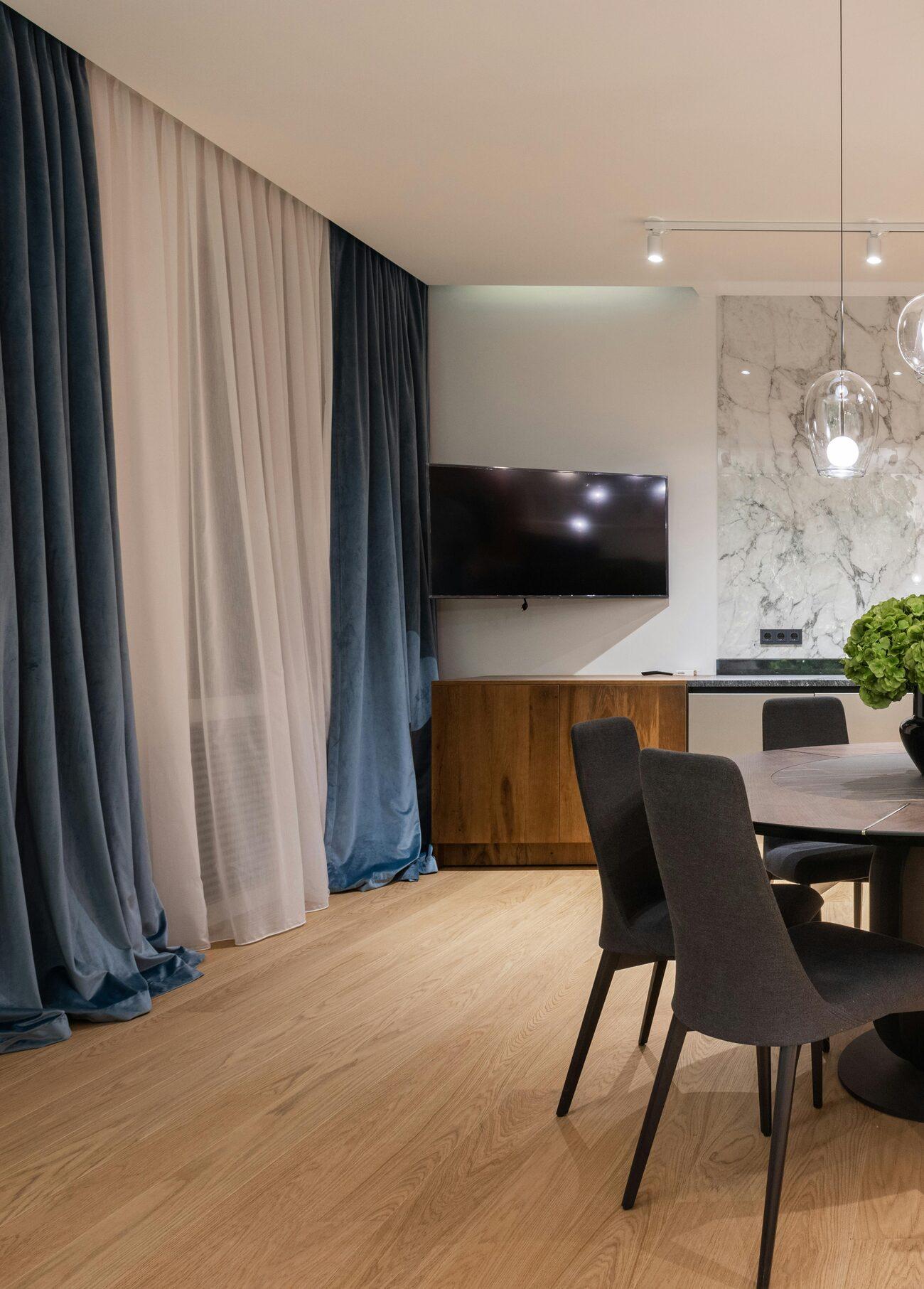Living and dining space dressed with deep blue velvet curtains over soft white sheers